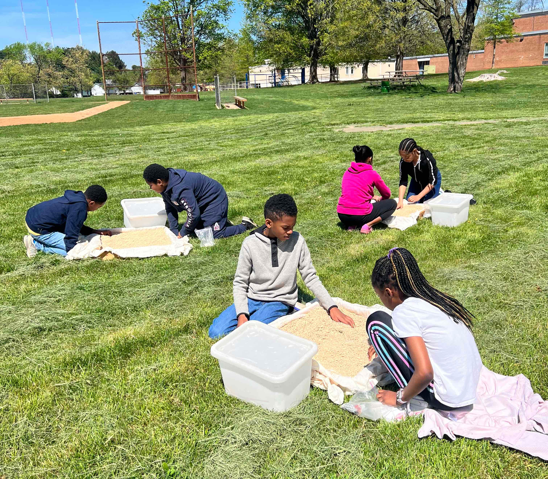 In pairs, Black elementary schoolers explore pans of sand and dirt as part of an archaeology course