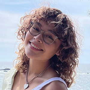 Jazmín Romero smiles with their head tilted to the side with the ocean in the background