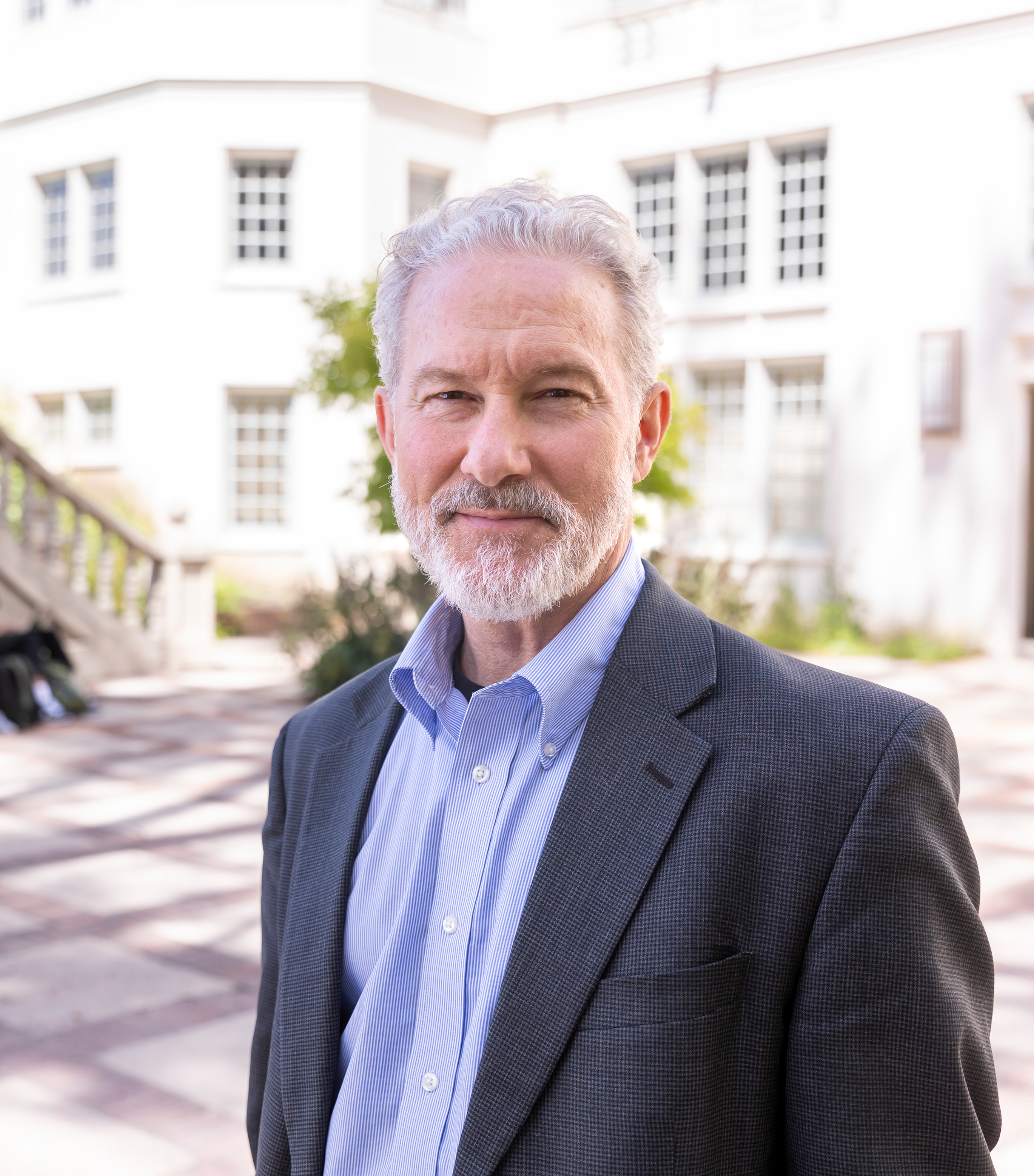 White male with white hair and a white beard smiles at camera on Berkeley campus
