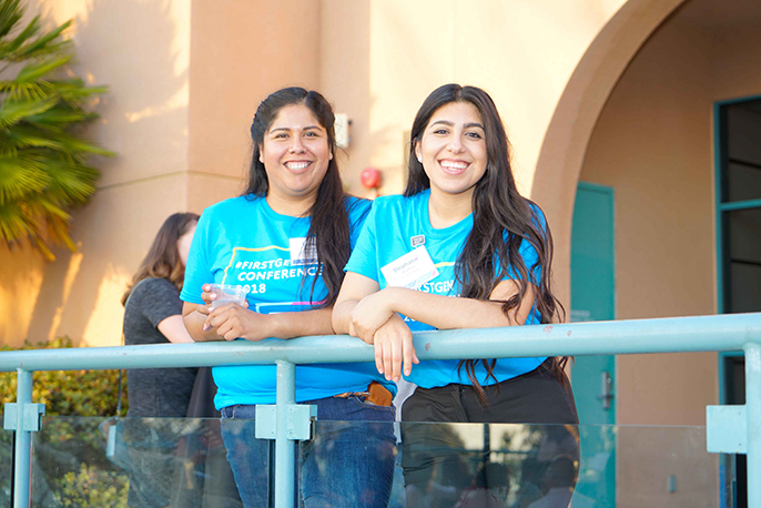 Two attendees of the First Generation conference smiling and leaning on a railing