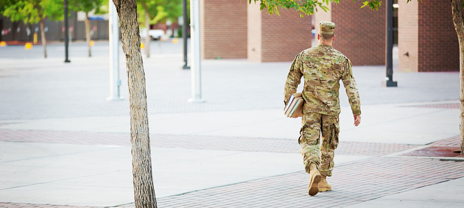 Soldier walks across a campus holding books