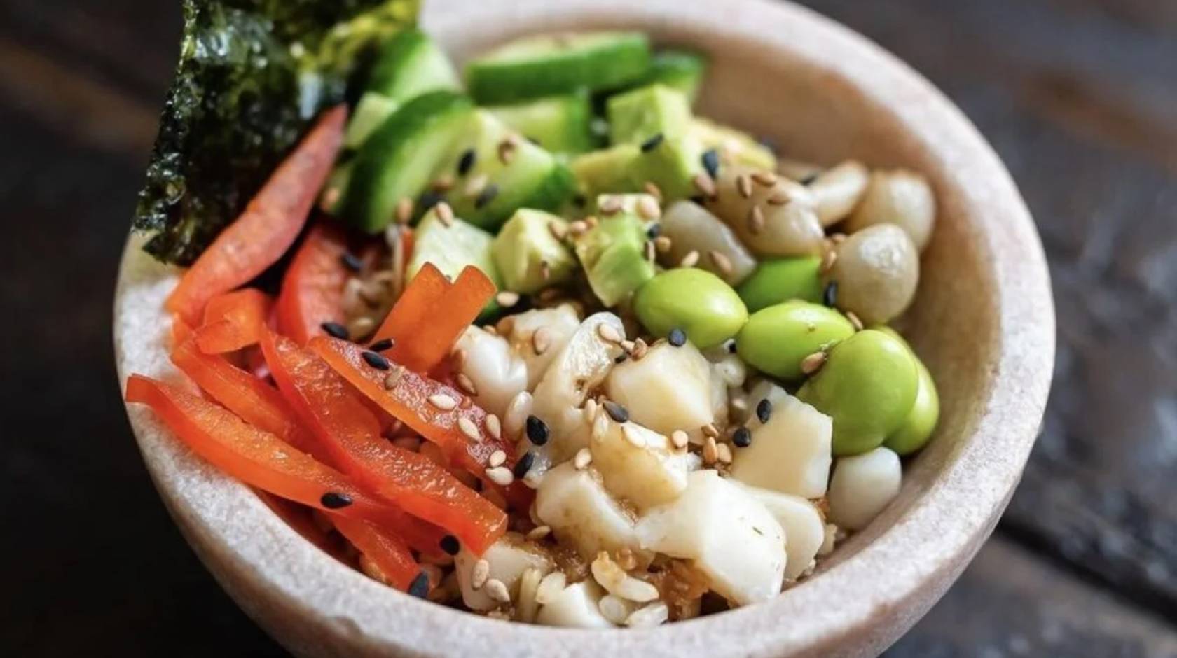 A poke bowl with vegetables, edamame, fish, sesame seeds and seaweed