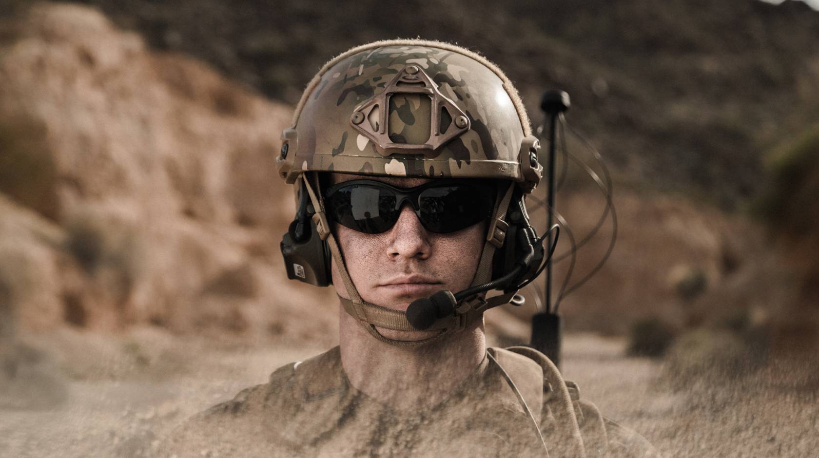 A man with sunglasses in military gear, in a desert