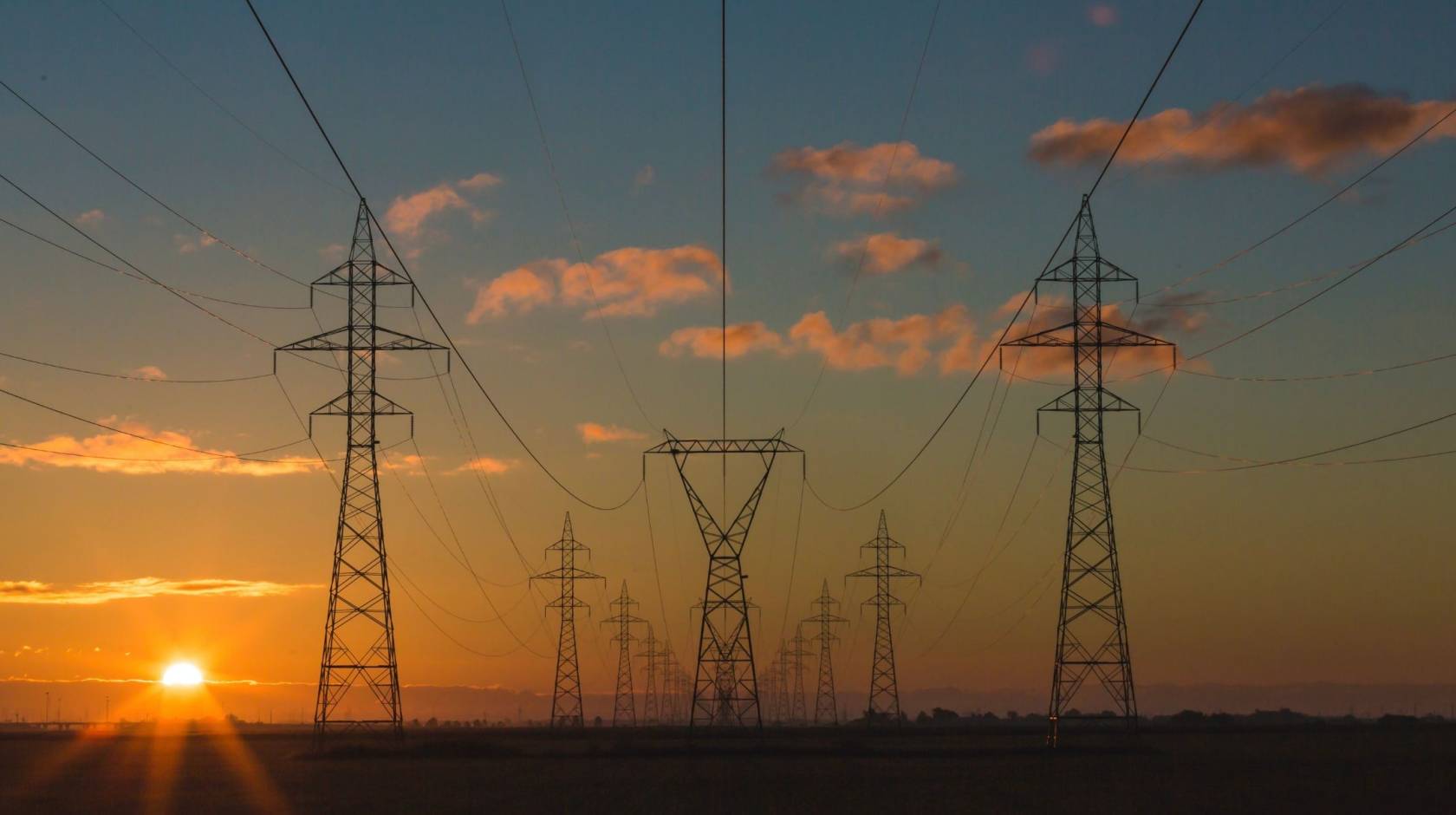 A hazy sunset behind electrical transmission towers, composed symmetrically in frame
