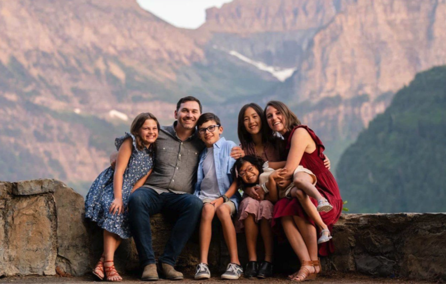 The Finlayson family, a man, woman and 4 kids, poses for a photograph in front of a mountain landscape.