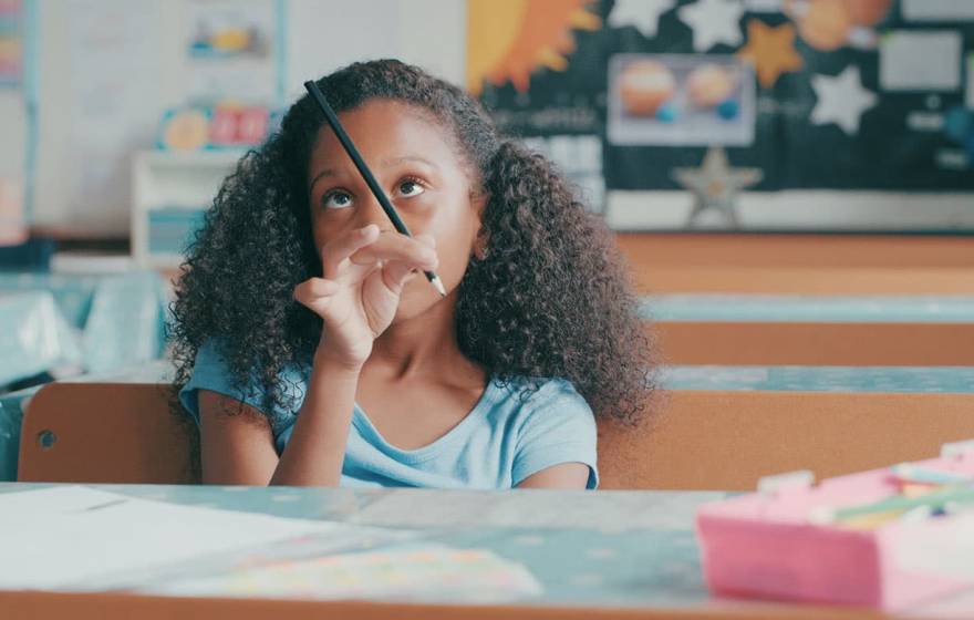 Young Black girl in classroom playing with her pencil, bored
