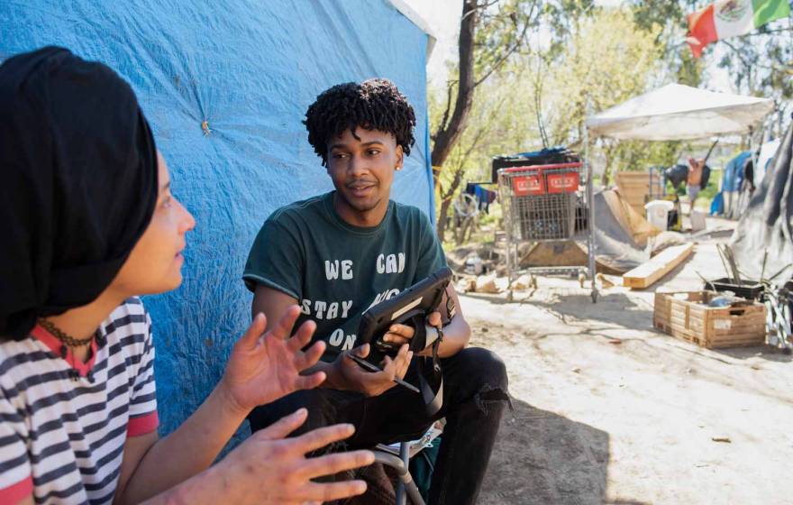 Young, attentive Black man listens to a woman in a homeless encampment and takes notes on a tablet