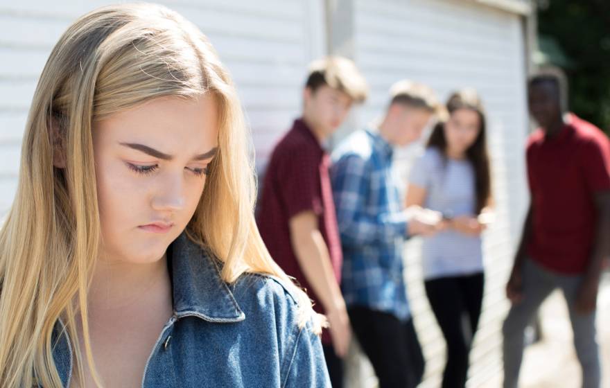 Blonde teenage girl frowns as peers behind her gossip