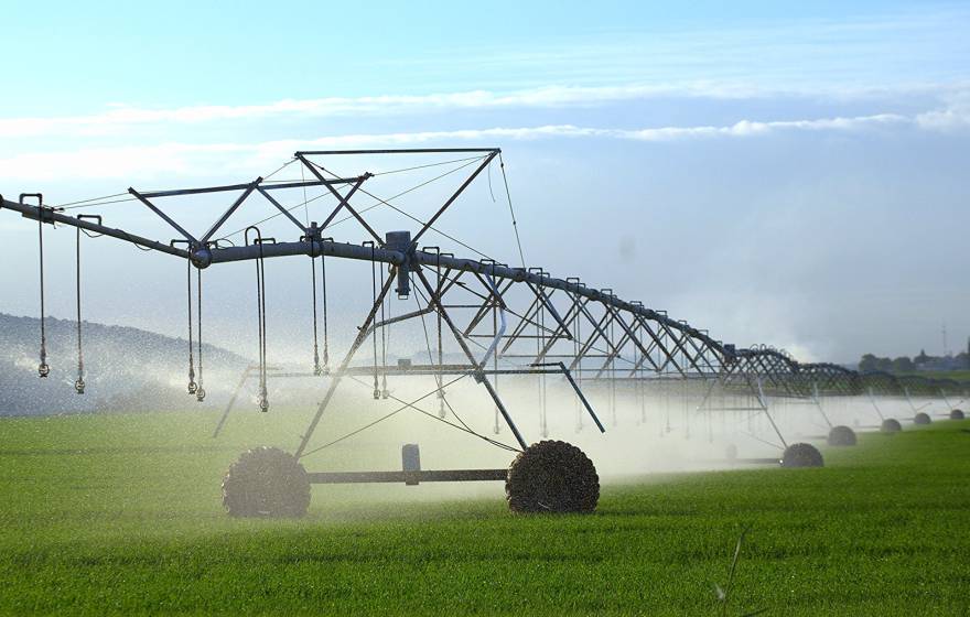 A spray irrigation system of metal irrigation equipment on a green field with mountains and clouds in the background