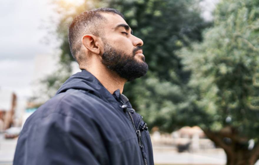 Young hispanic man with eyes closed taking a deep breath outside