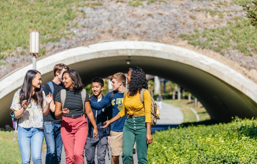 Diverse small group of happy students walking away from an arch on UC Irvine campus