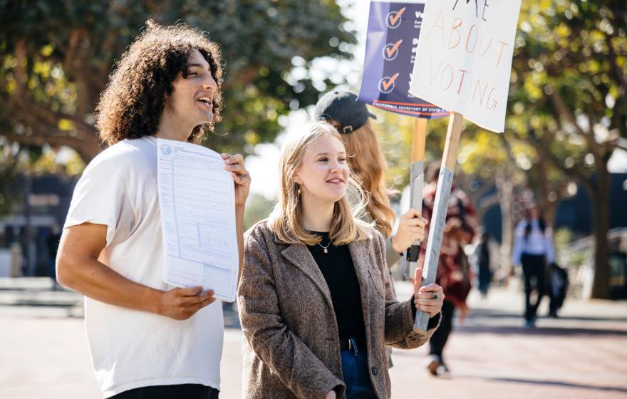 Alex Edgar and Skylar Betts hold up signs to encourage students to register to vote on the UC Berkeley campus
