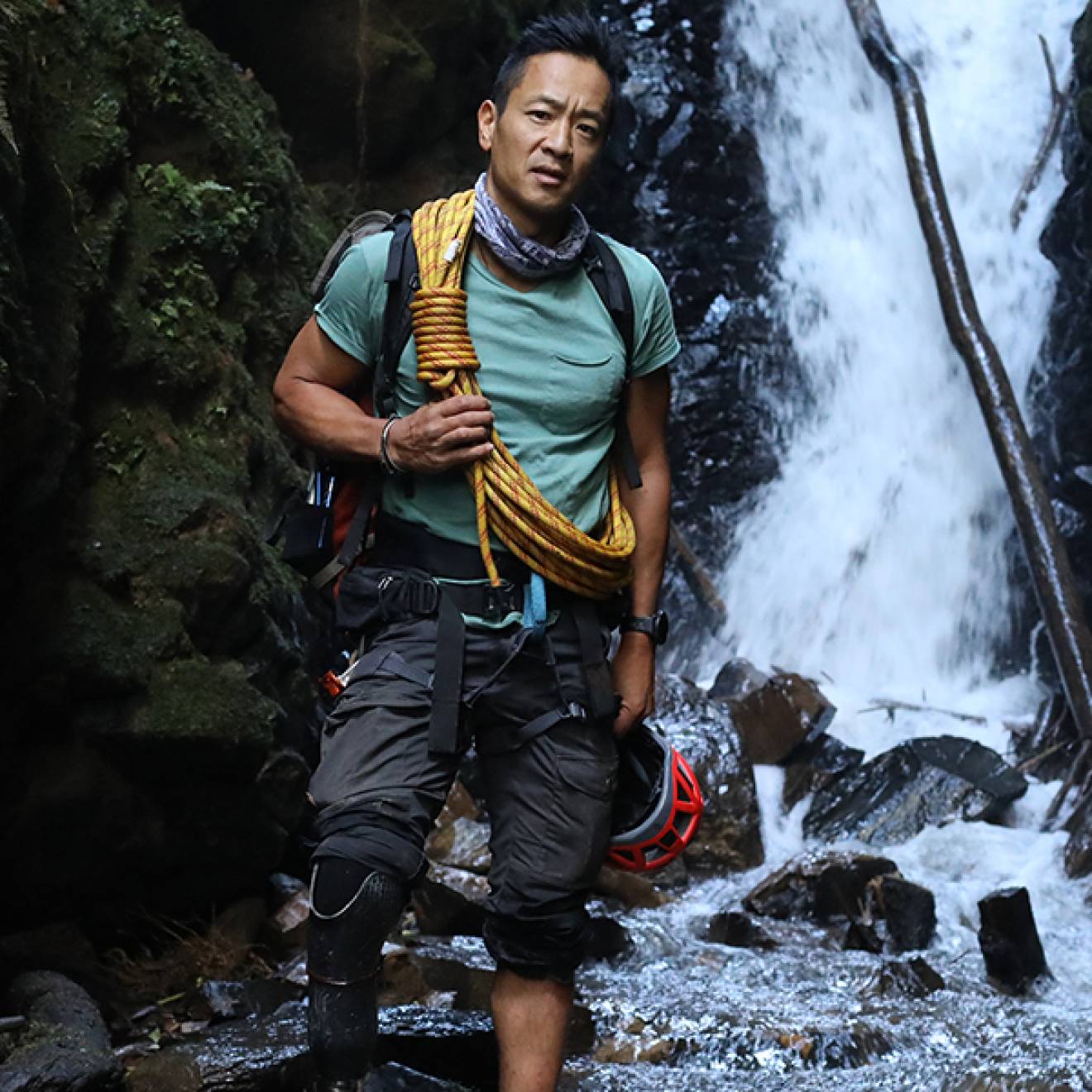 Albert Lin in outdoorsy gear stands in front of a waterfall