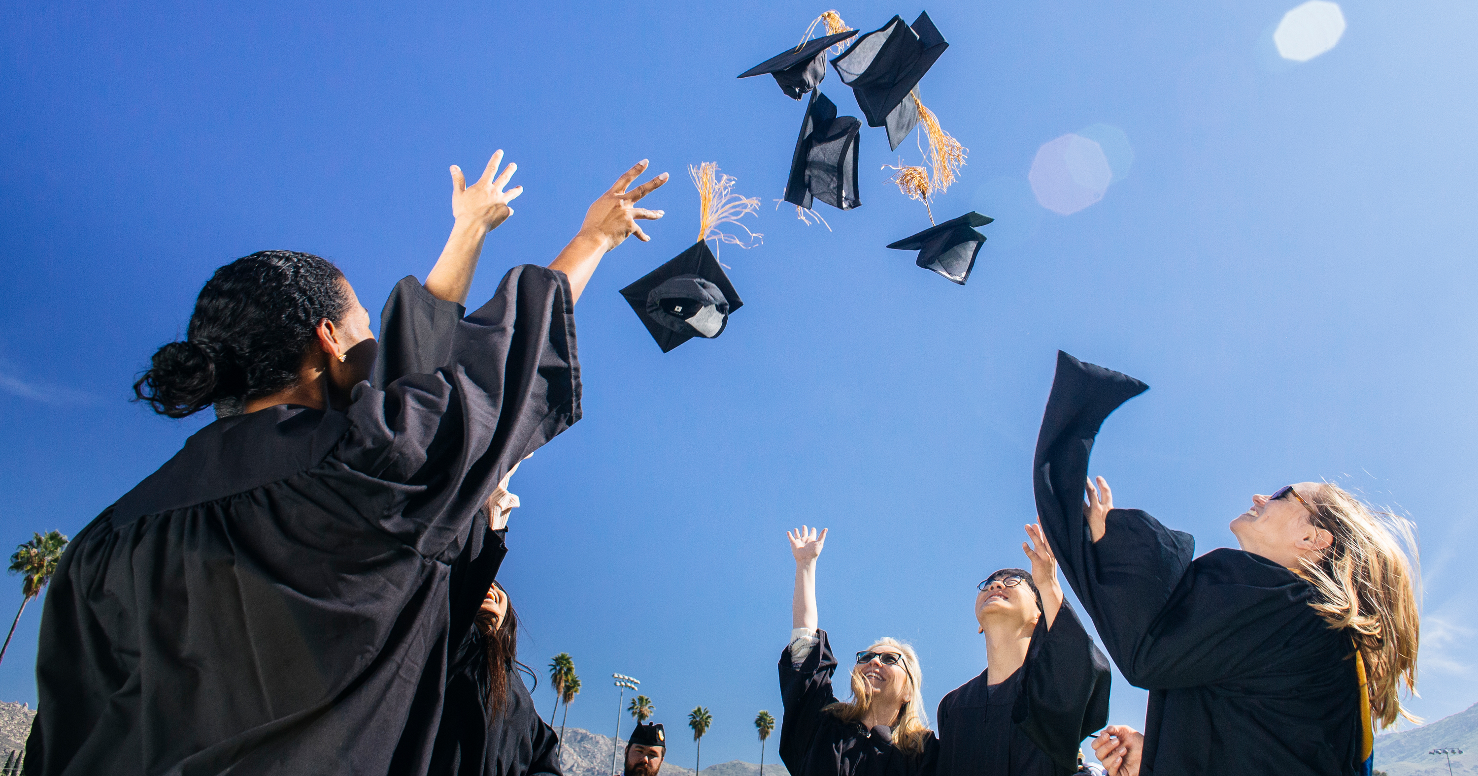 College graduates in black robes throwing their caps in the air against a blue sky