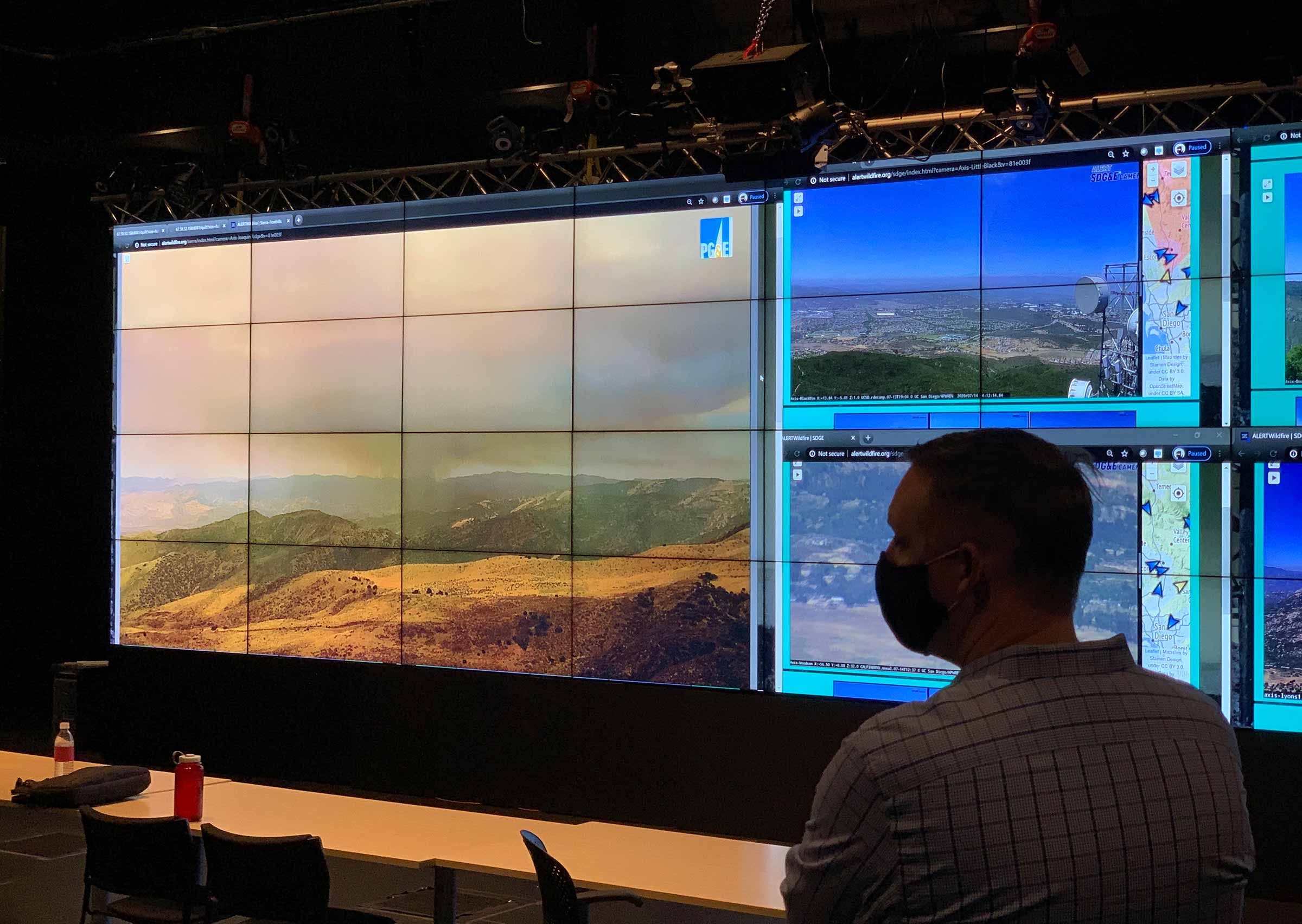 Man in mask looking at a giant screen of a wildfire smouldering