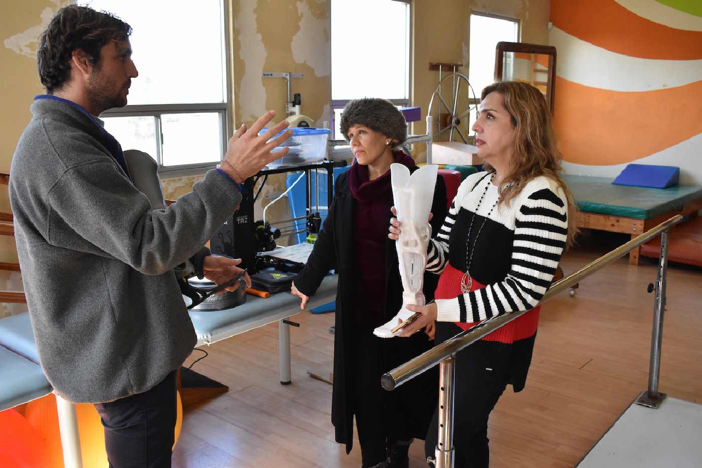 A man and two women talking, one of whom is holding a prosthetic