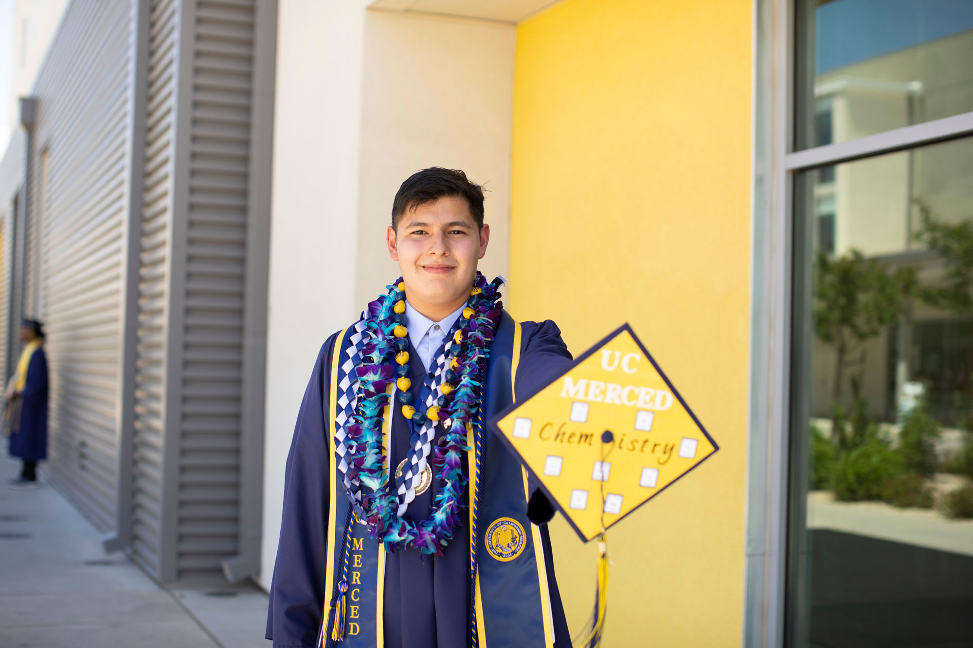 Anthony Alfaro in his gown and graduation stole, showing off his chemistry graduation cap