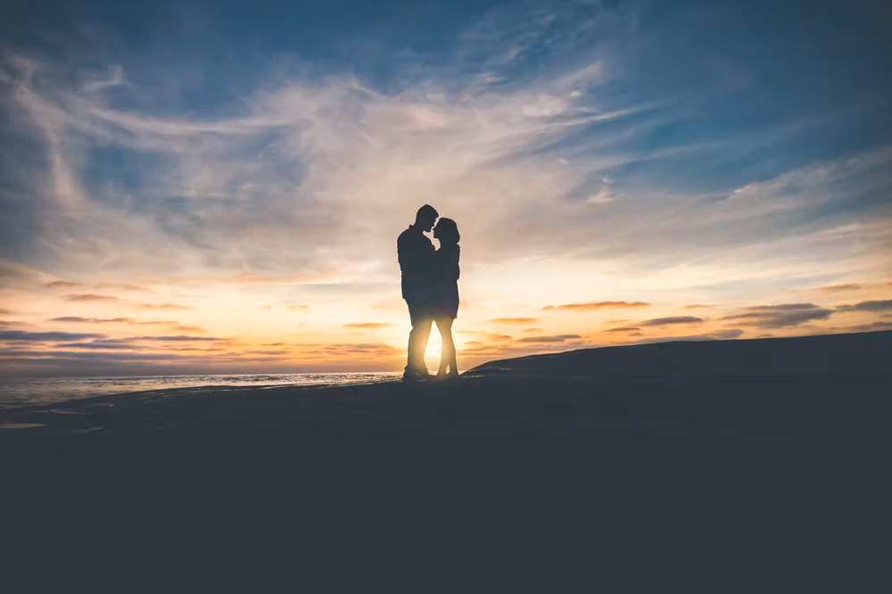 a couple embraces in front of a sunset