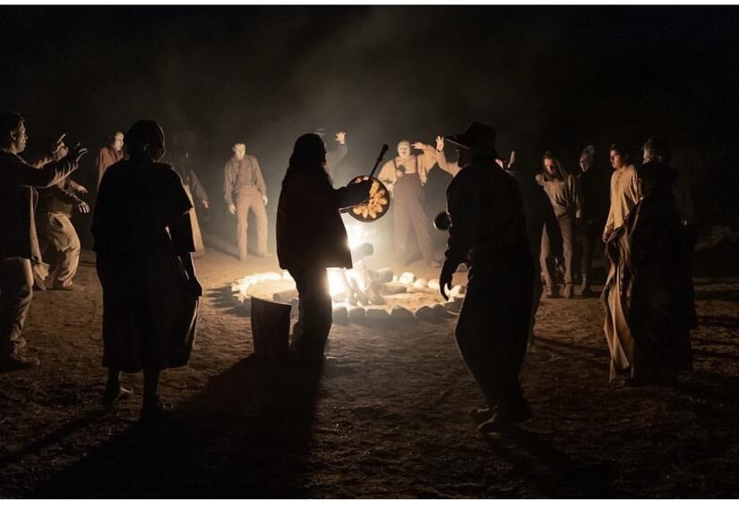 A group of men dancing around a fire, some faces whitened