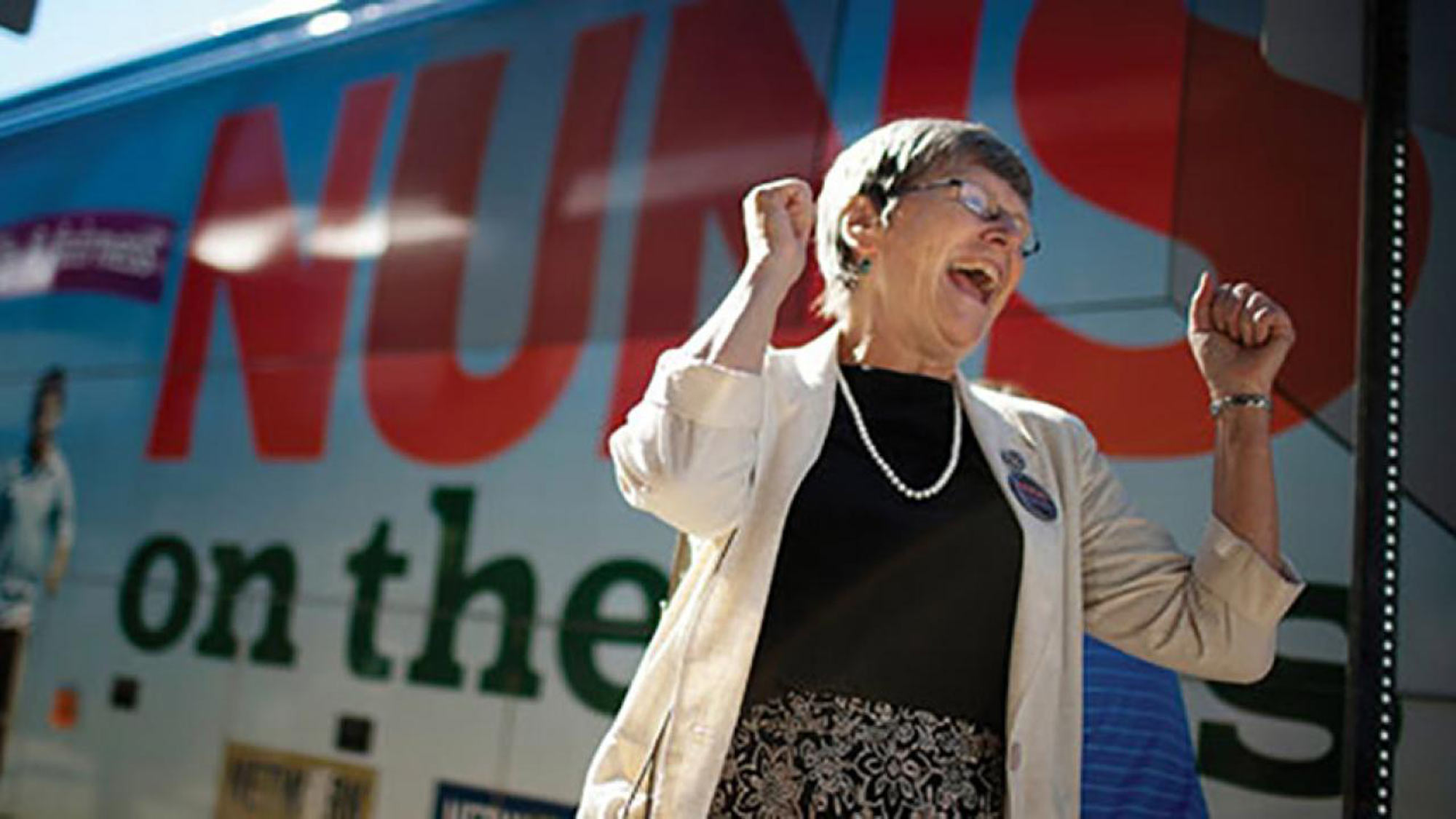 Sister Simone raising her fists in excitement in front of a bus