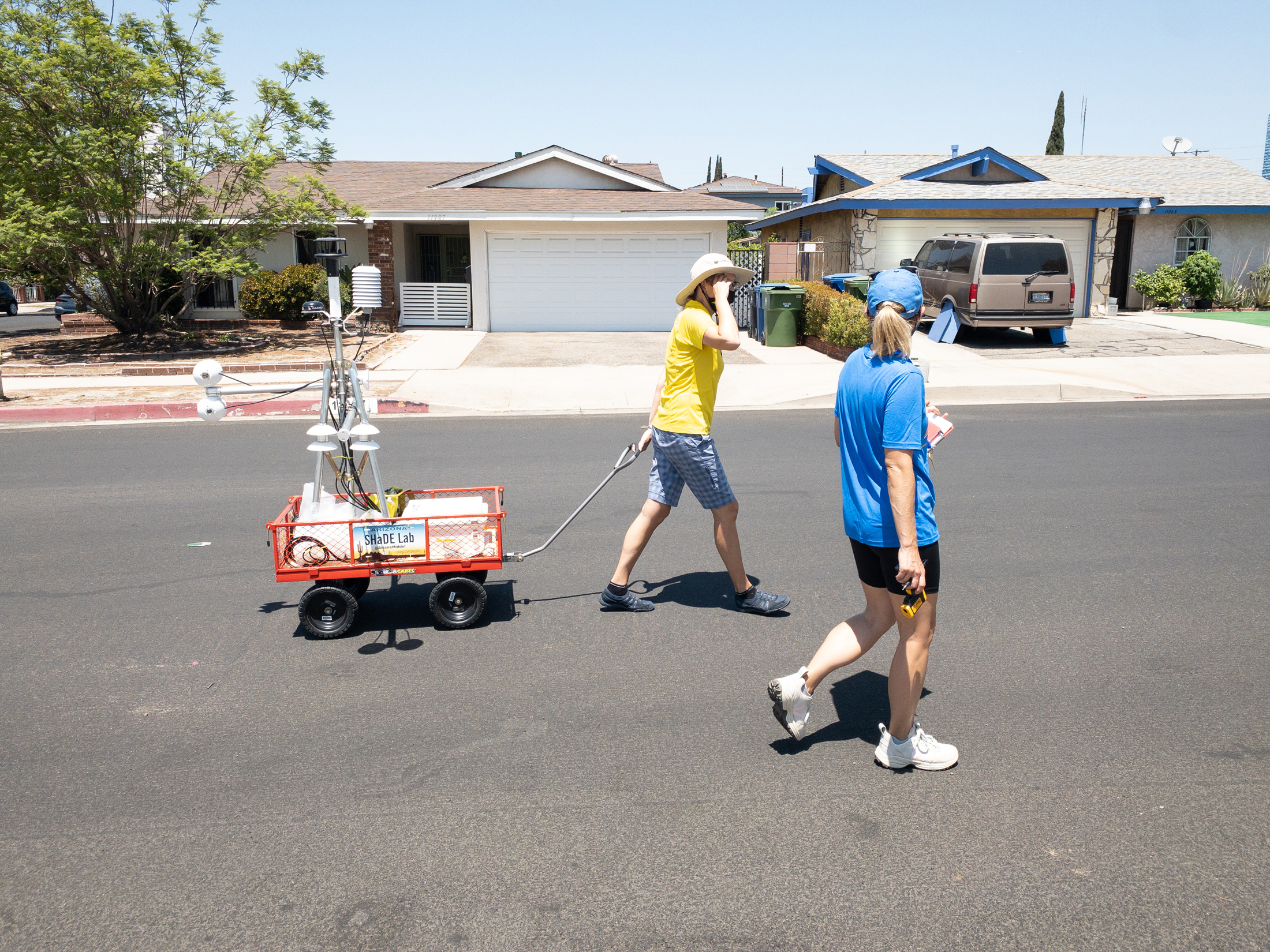 Two women walking through an urban neighborhood with heat measurement technology in a wagon