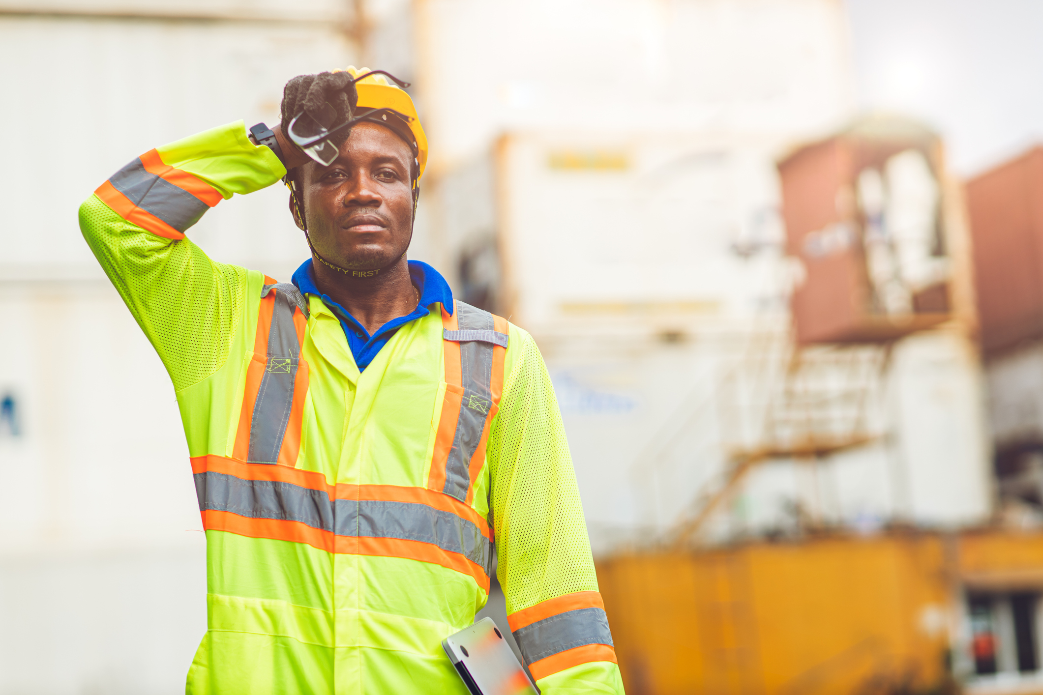 Black worker in yellow vest wiping away sweat