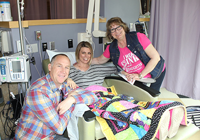 Michelle Brubaker in a hospital bed with her husband and mom surrounding her