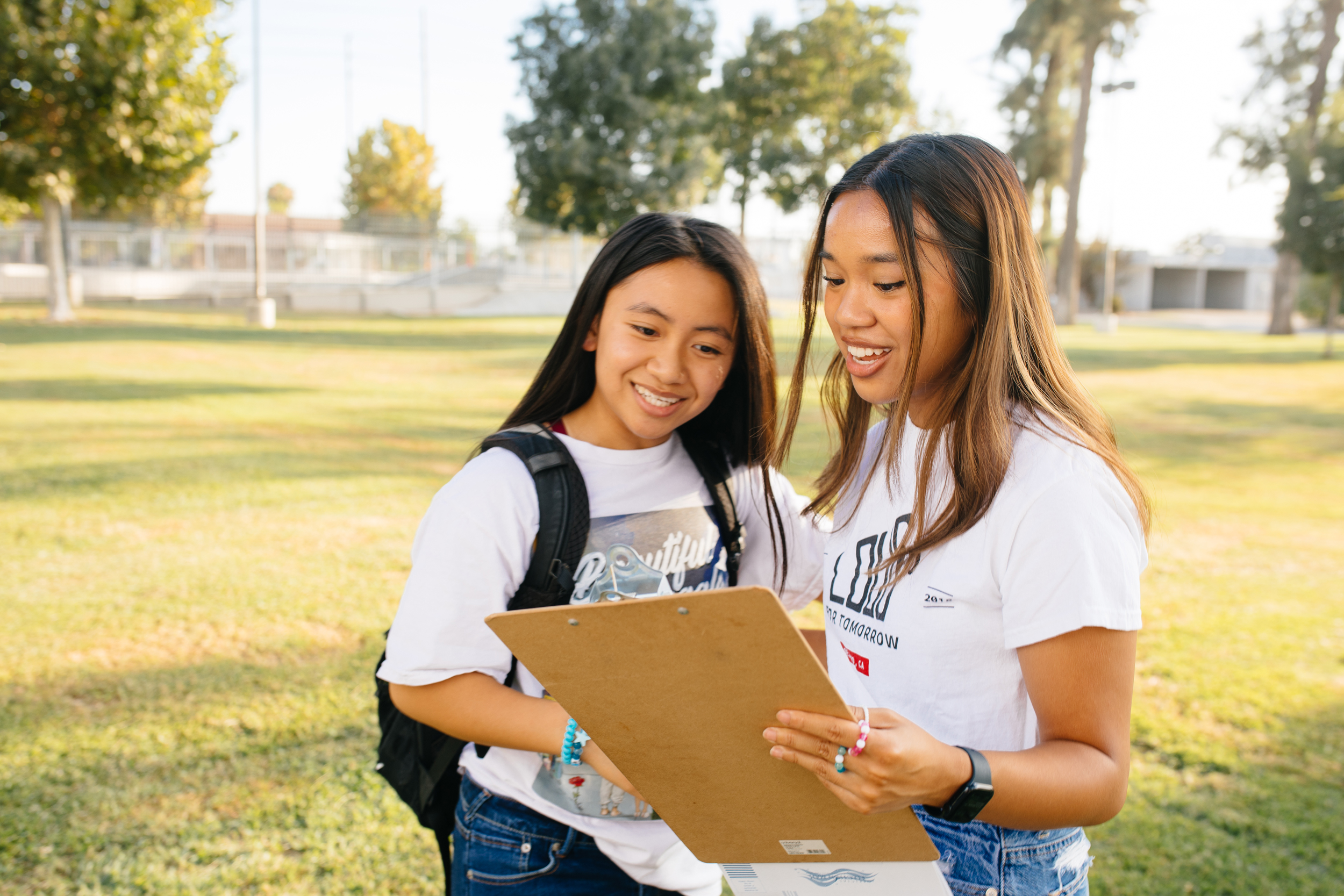 Two young women looking at a clipboard together outside