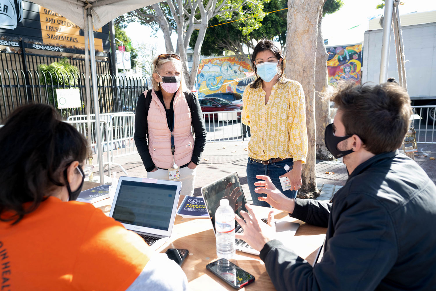 Four people talking in masks over a table outside