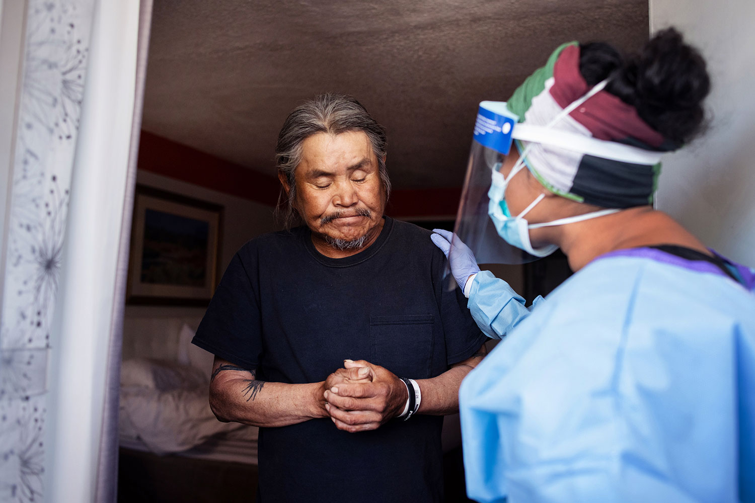 A woman in a mask and face shield visits a Navajo man