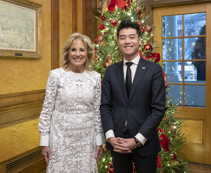 First Lady Jill Biden and Steven Gong standing together in front of a Christmas tree in formal clothes