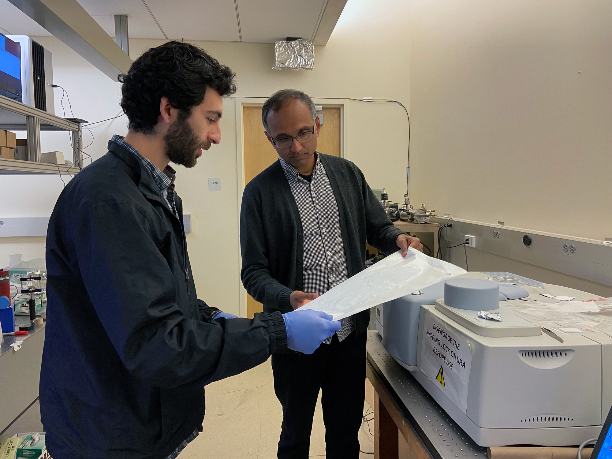 Two men hold a sample of a painted surface in an office hallway