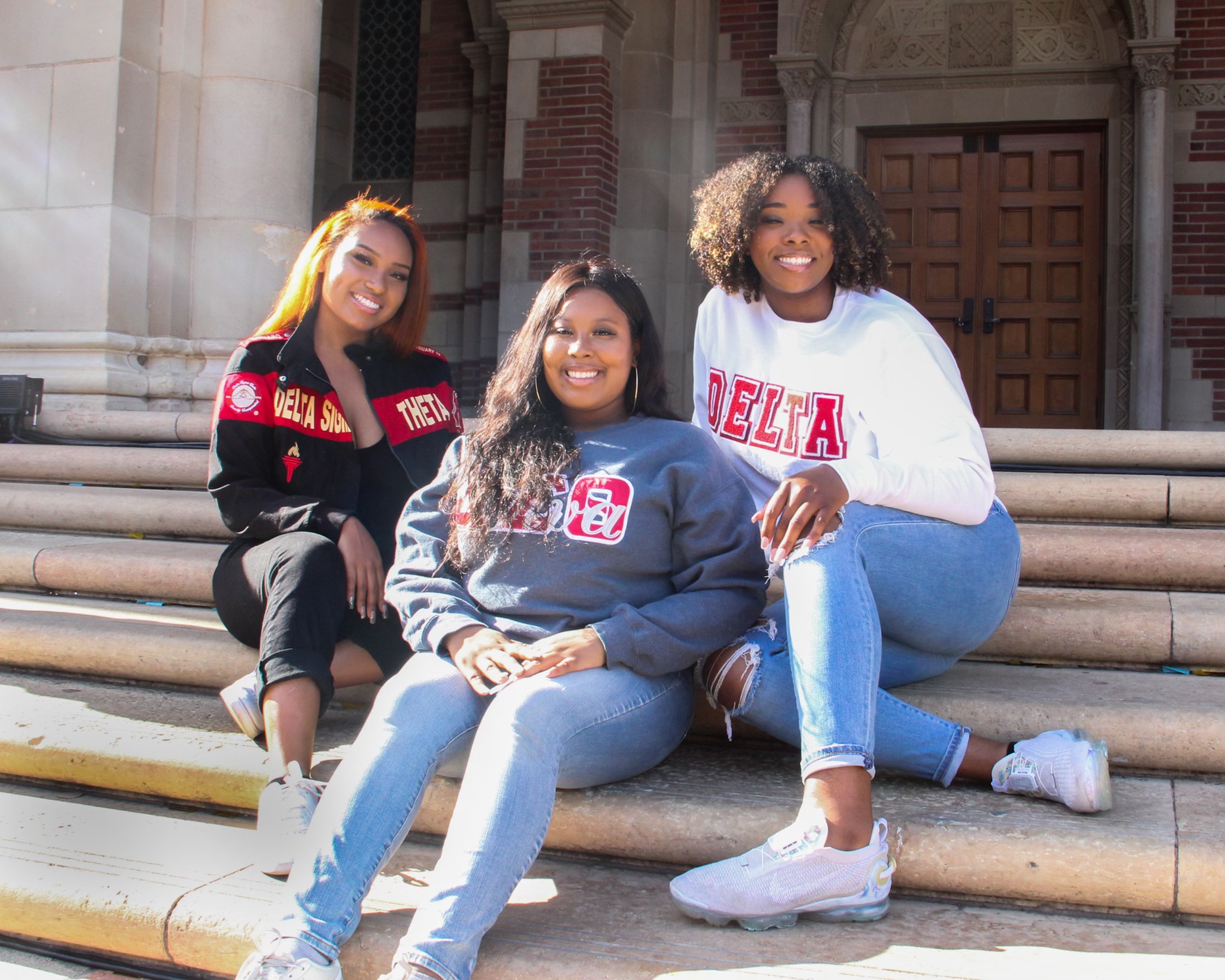 Three women posing in Delta sweatshirts, sitting on stairs