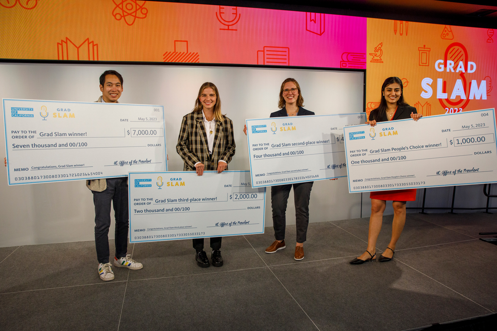 Brandon Tsai, Elissa Monteiro, Julia Mouat and Aneelman Brar on the Grad Slam stage, holding giant checks