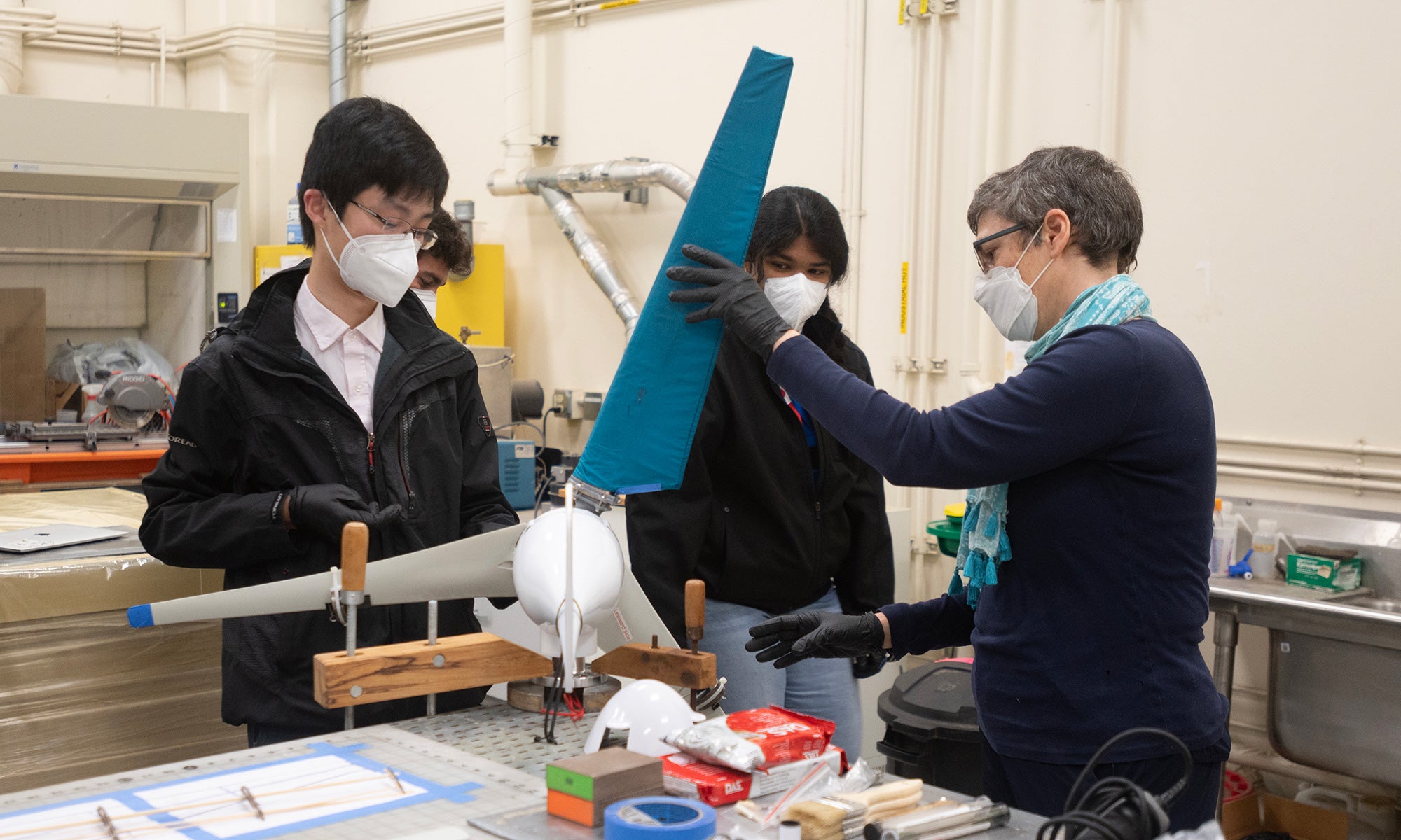 Three people, two women and a man, working on a turbine together with masks in a lab