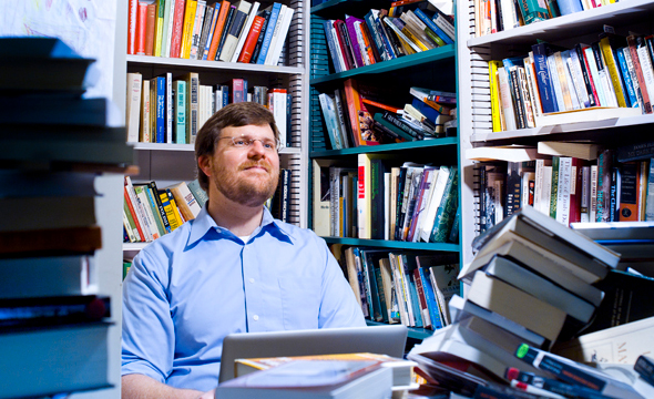 A white man with a goatee looking up in an office covered with bookshelves