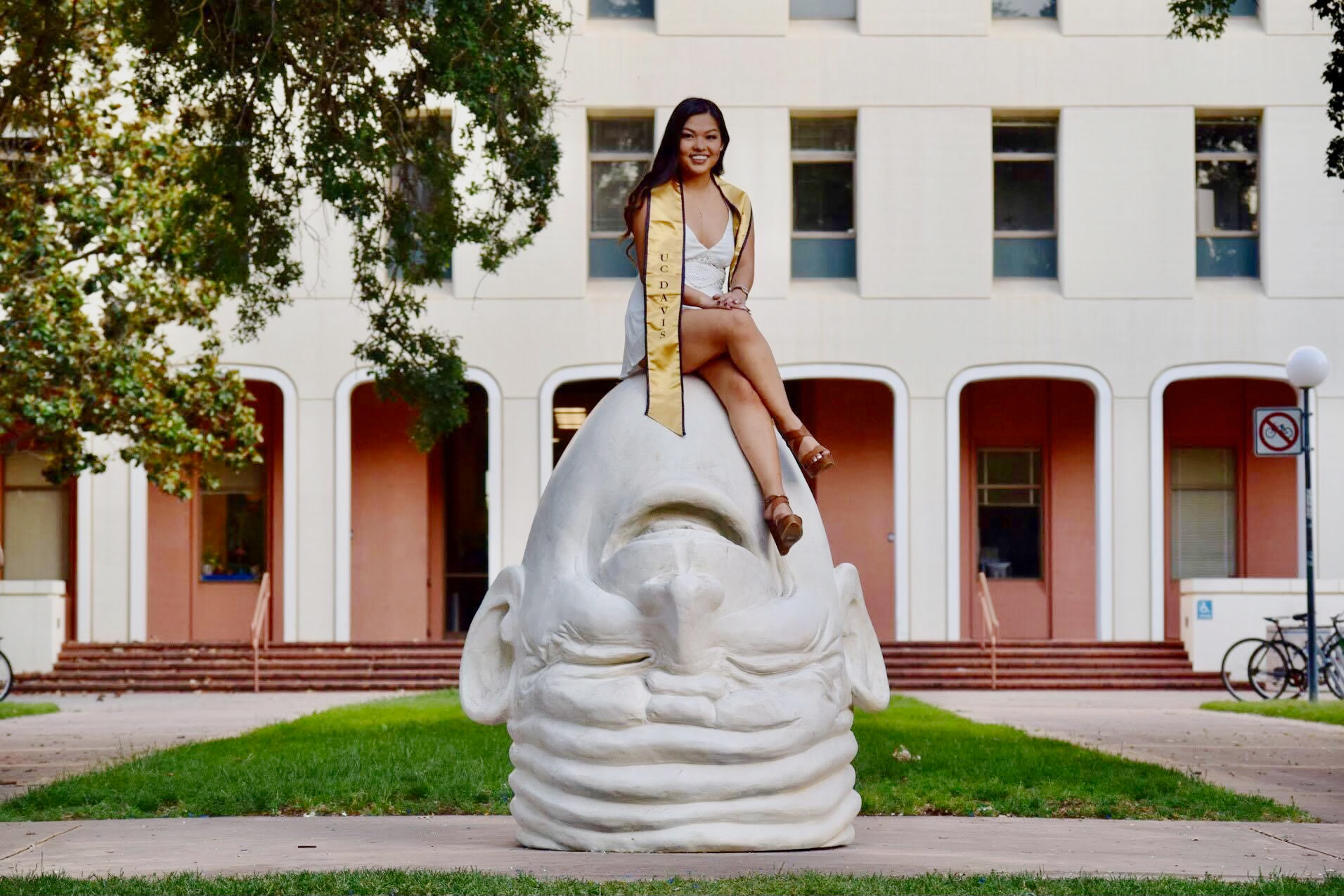 A person wearing a graduation sash sitting on top of a large outdoor sculpture