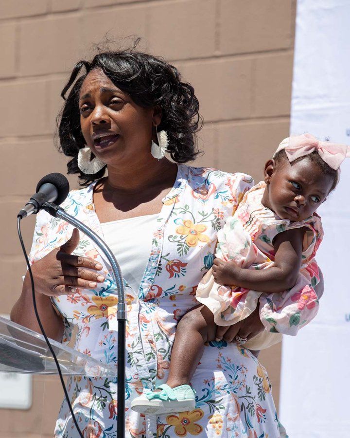 A Black woman speaks at a mic outside while holding her baby