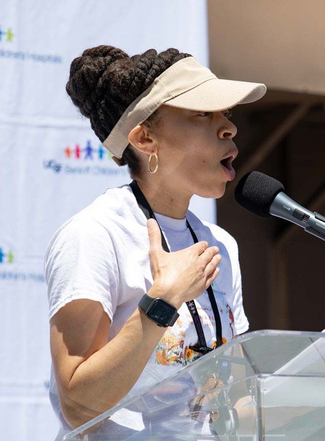 A Black woman wearing a visor speaks at a mic outside