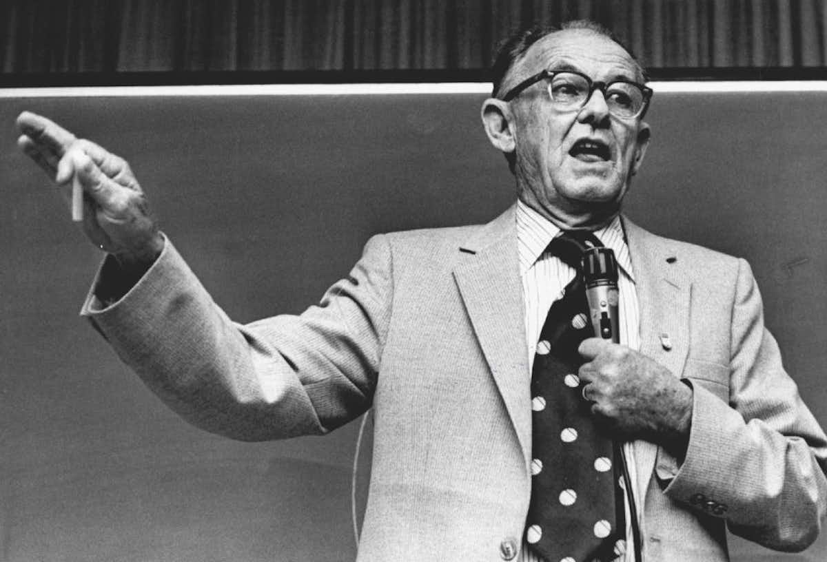 An older, balding man in a suit pointing while talking on a mic