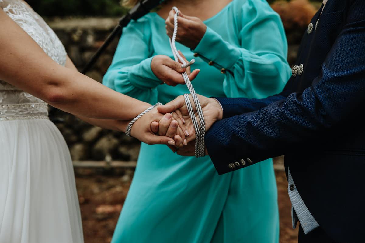 A woman in a dress tying a bride and groom together with an actual string
