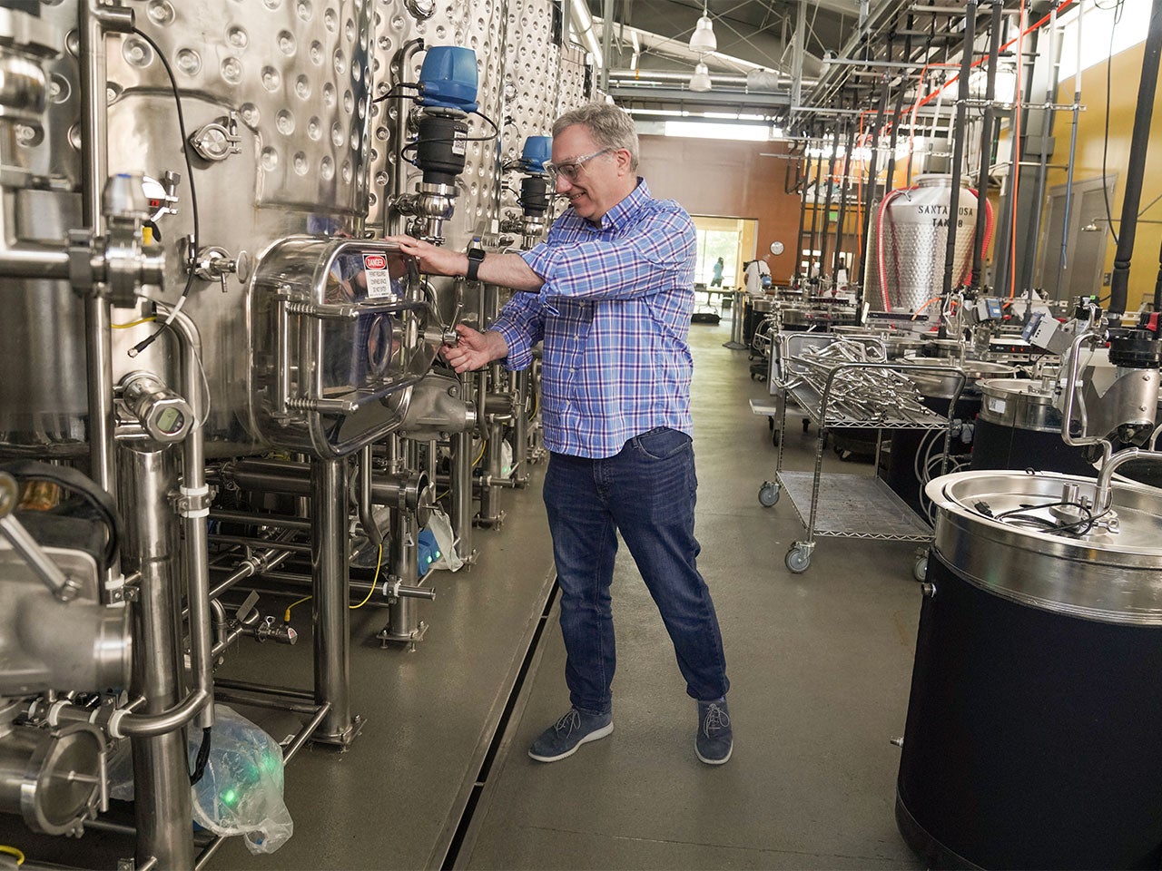 An older man twists a knob on a big metallic fermentation tank