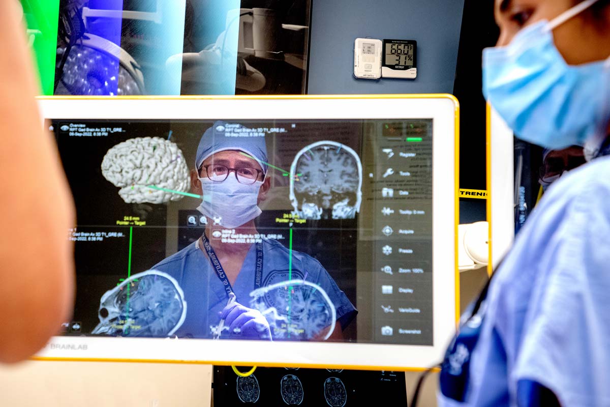 Edward Chang mid-surgery in the reflection of a screen with multiple brain illustrations on it