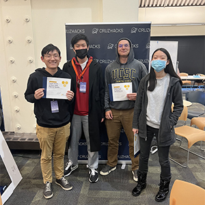 Three young men, one in a mask, and one young woman, in a mask, holding certificates showing their contest win