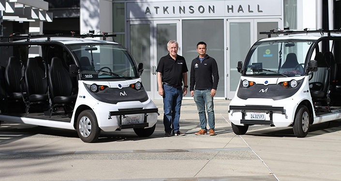 two people standing next to two autonomous vehicles