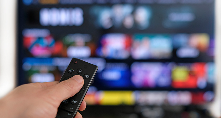 a hand with a remote control pointed at a TV screen