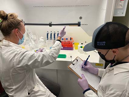 A teenage boy working in a lab with an adult female supervisor, both in PPE