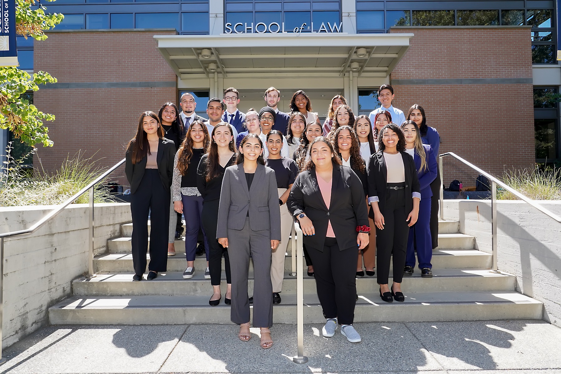 A group of young men and women in professional clothes and blazers posing on stairs outside the UC Davis School of Law