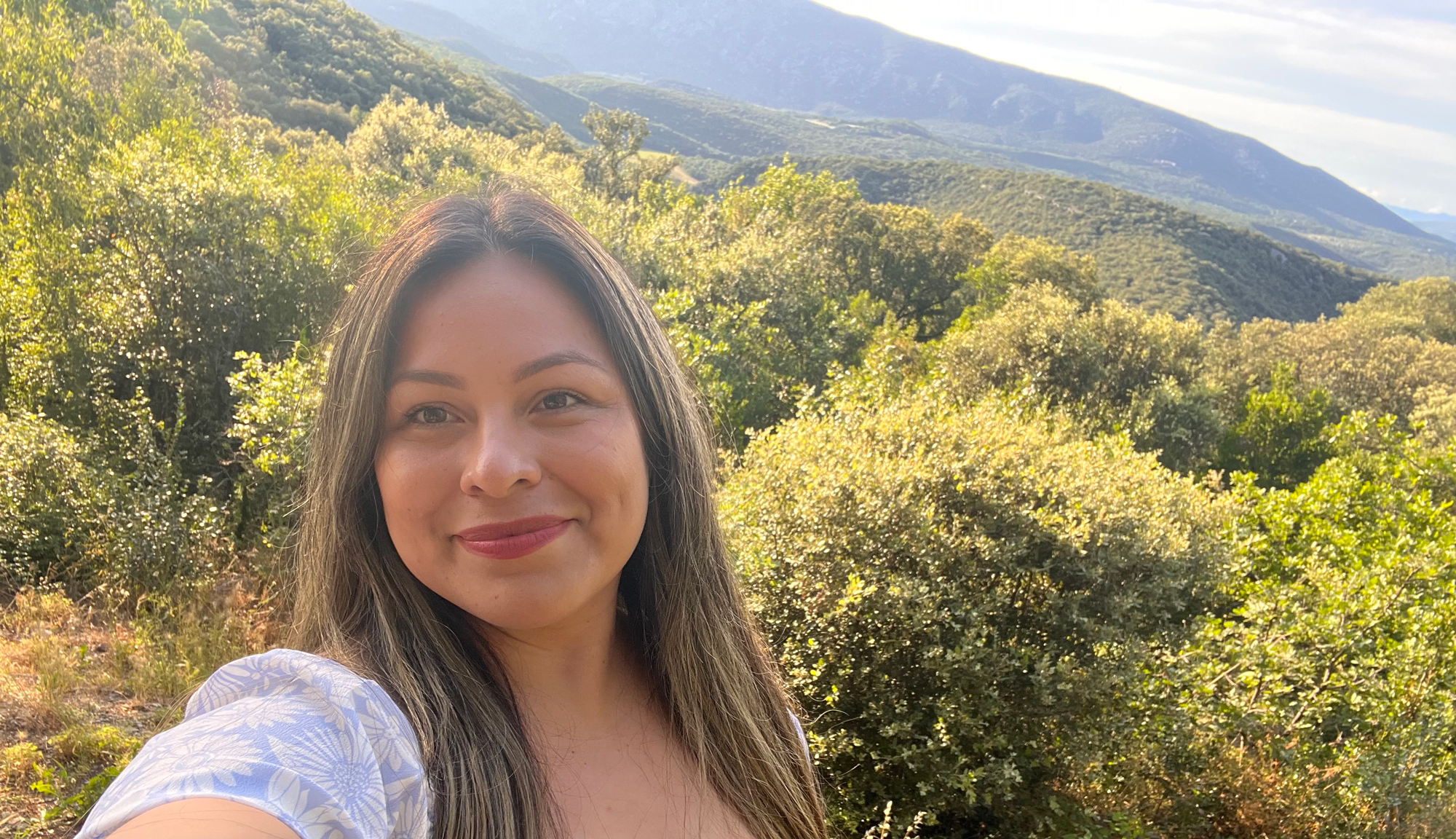 A woman taking a self-portrait in a natural setting with hills in the distance