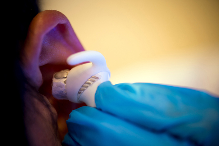 Blue gloved fingers insert a white earbud into an ear